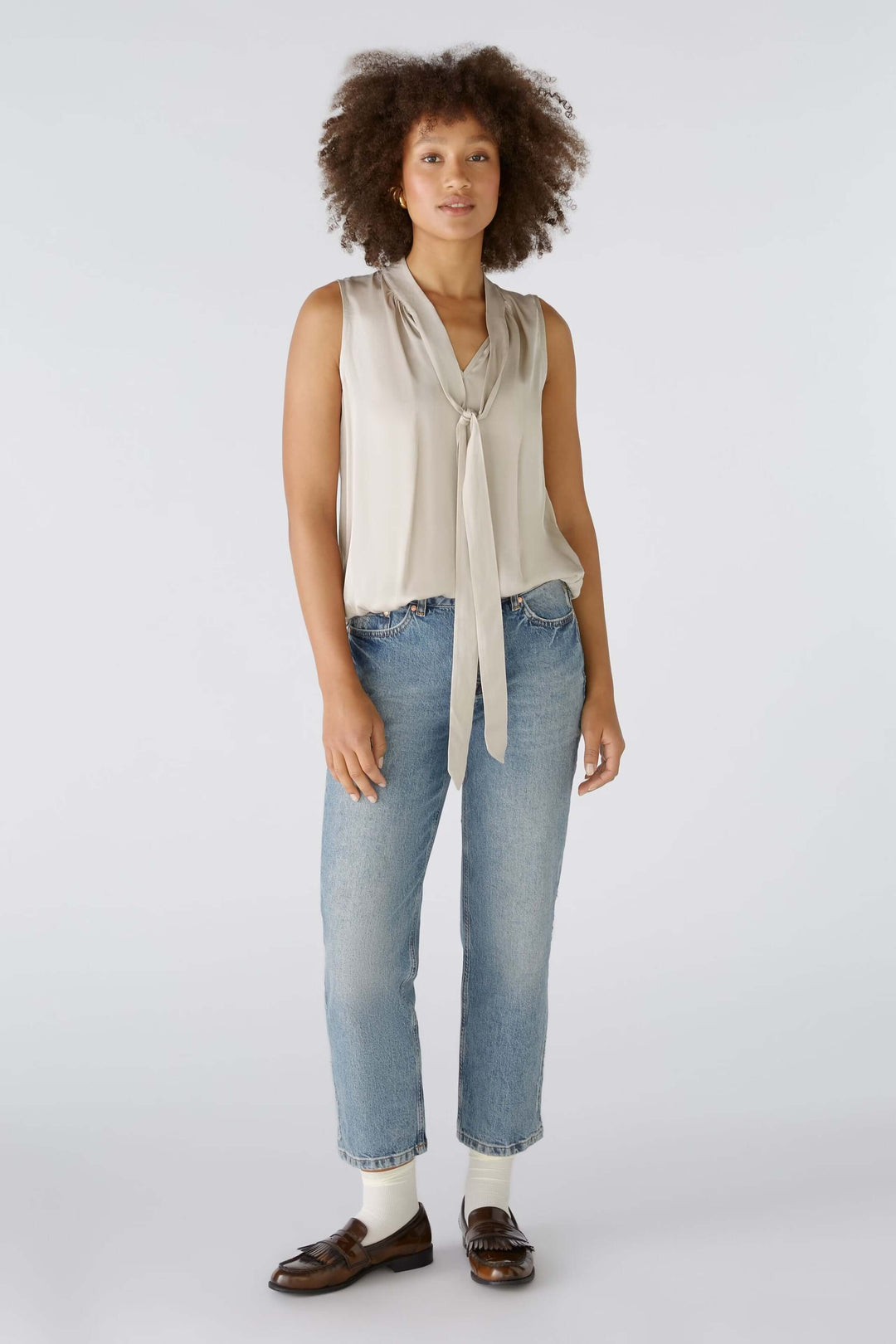 Femme portant une blouse évasée satinée avec un col en V, ceinture élastiquée et volants, mise en valeur par un jean décontracté.