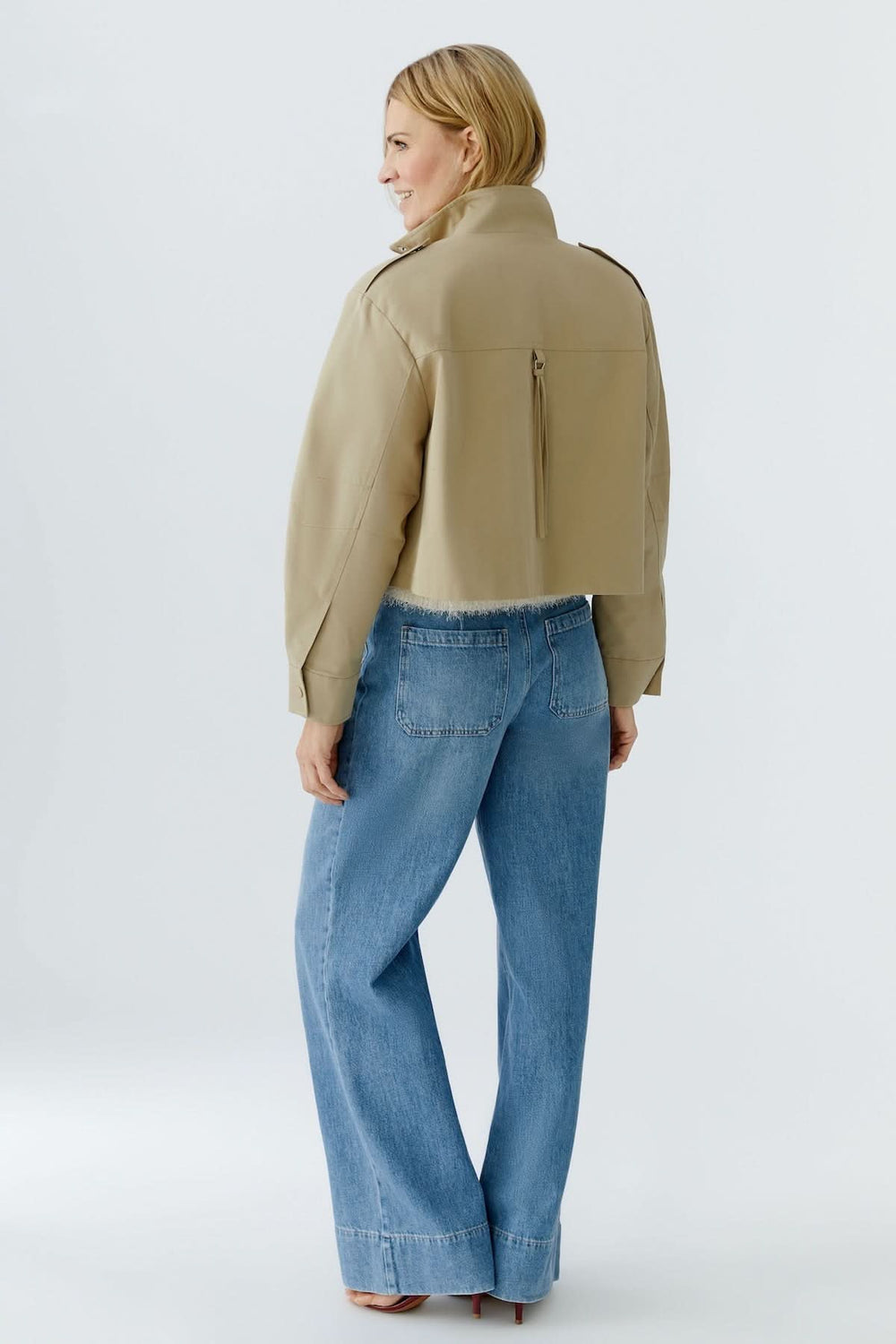 Blouson court à col montant structuré beige porté par une femme de dos, associé à un jean large pour un look moderne.
