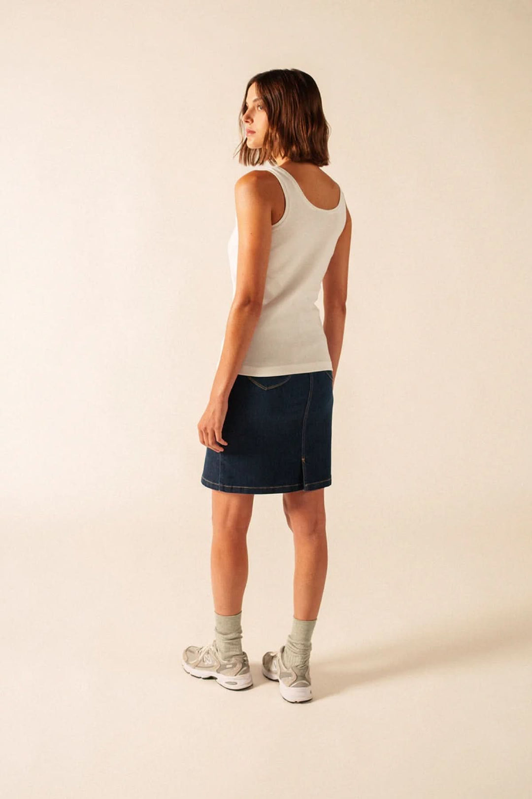 Femme portant Camisole Bastia ajustée à encolure arrondie, vue de dos, avec jupe en denim et baskets grises, tenue décontractée et confortable.