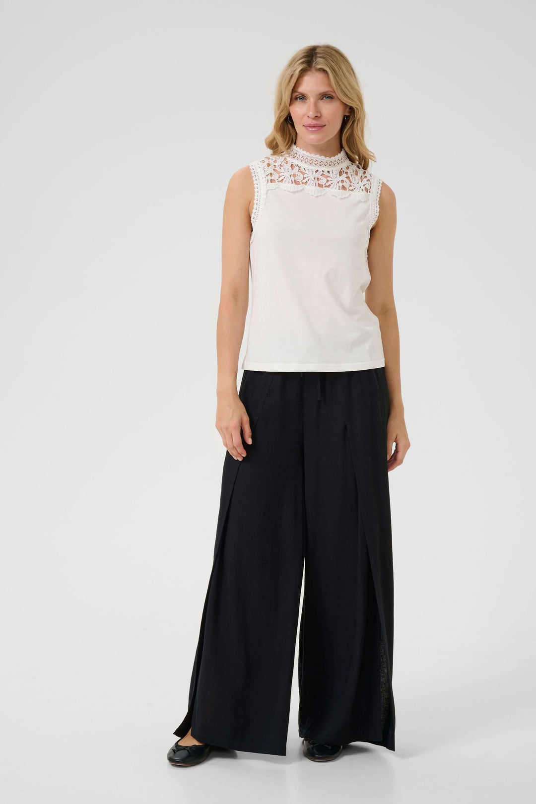 Camisole Livy blanche à dentelle au col, accompagnée de pantalons larges et élégants, pour un look sophistiqué.