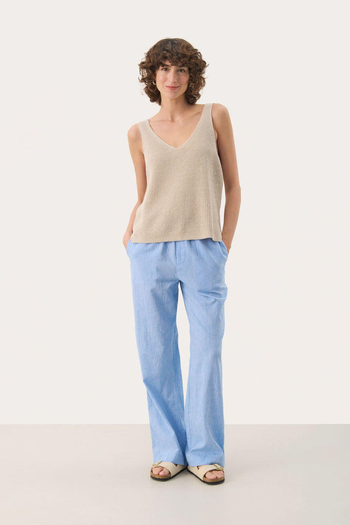 Femme portant la Camisole Rebecca tricotée col v sans manches beige avec pantalon bleu, allure décontractée et naturelle.