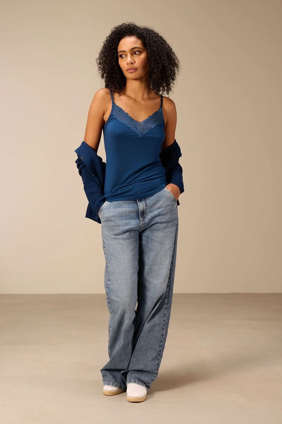 Femme portant une camisole à bretelles avec dentelle en bleu, associée à un jean et une veste, soulignant la féminité et le confort.