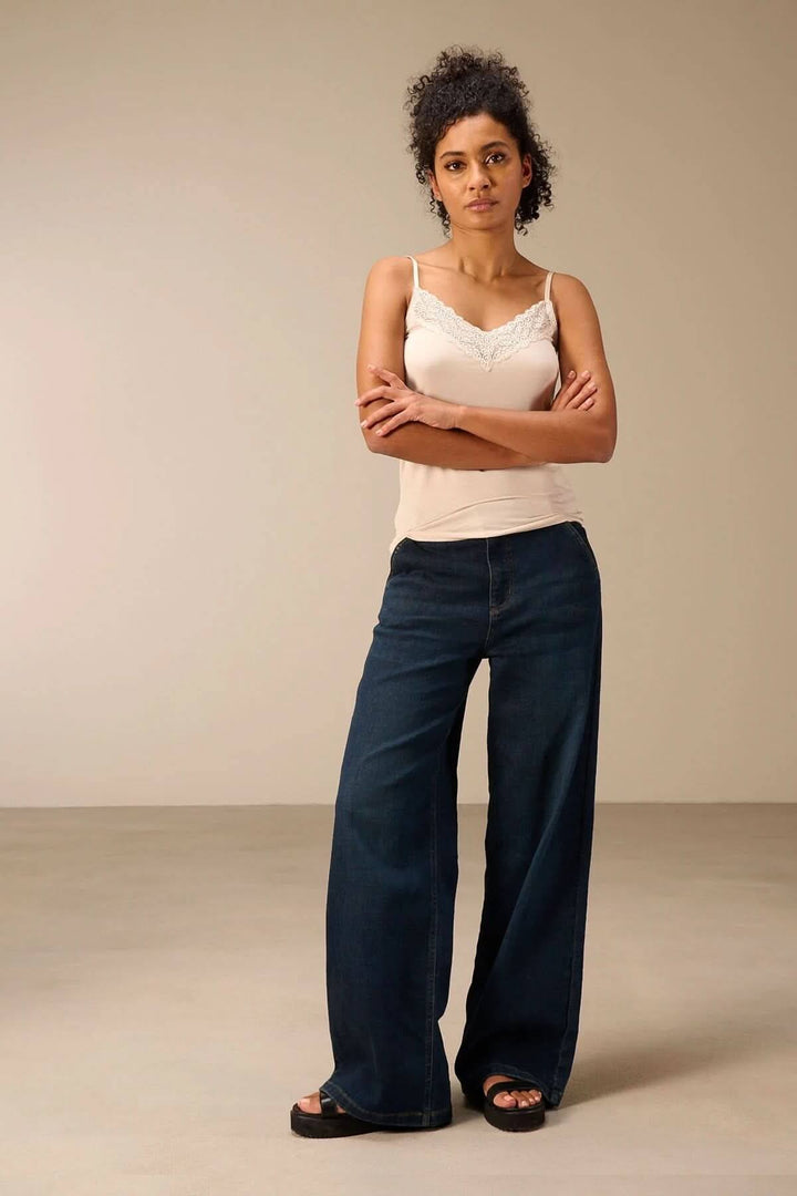 Femme portant une camisole à bretelles avec dentelle, idéal pour un look chic et polyvalent, associé à un jean large.