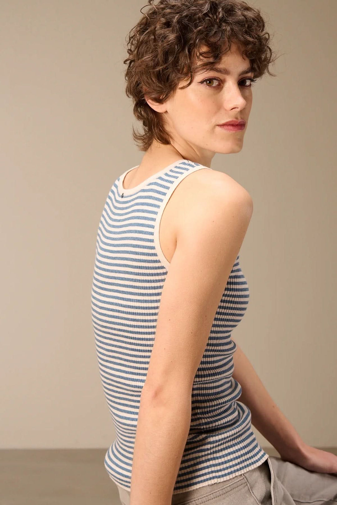 Femme portant une camisole côtelée rayée col rond, dos tourné, avec des bretelles larges et une coupe ajustée, parfaite pour un look estival.