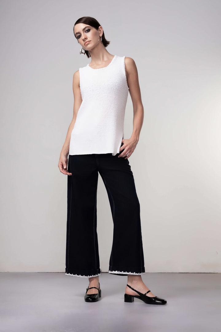 Femme portant une camisole en maille blanche élégante avec un pantalon noir, tenue minimaliste idéale pour superposition.