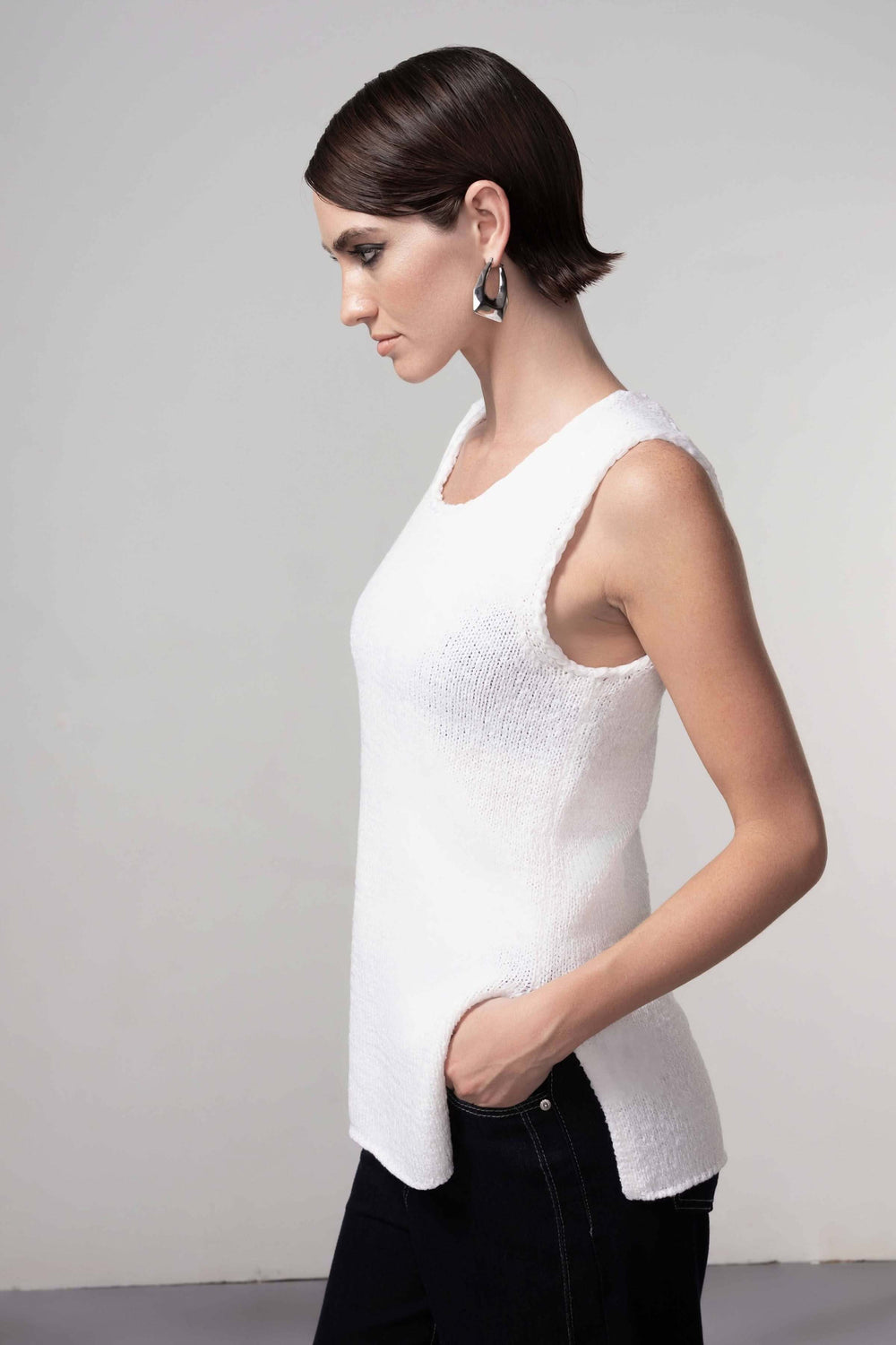 Femme portant une camisole en maille blanche, silhouette épurée, encolure arrondie, coupe droite légèrement allongée.