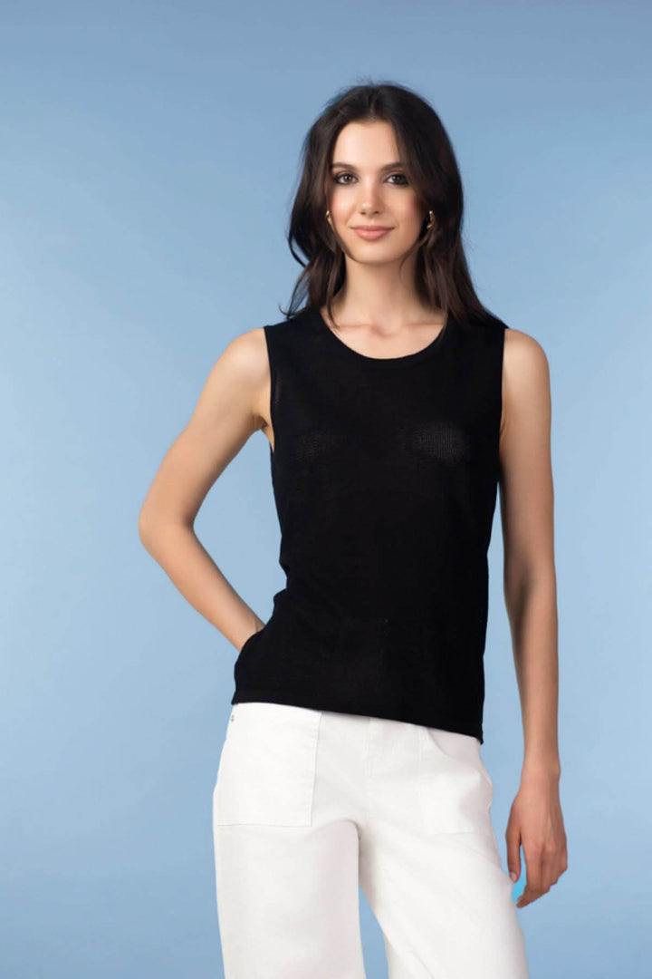 Femme portant une camisole en maille texturée noire avec pantalon blanc, style moderne et épuré.