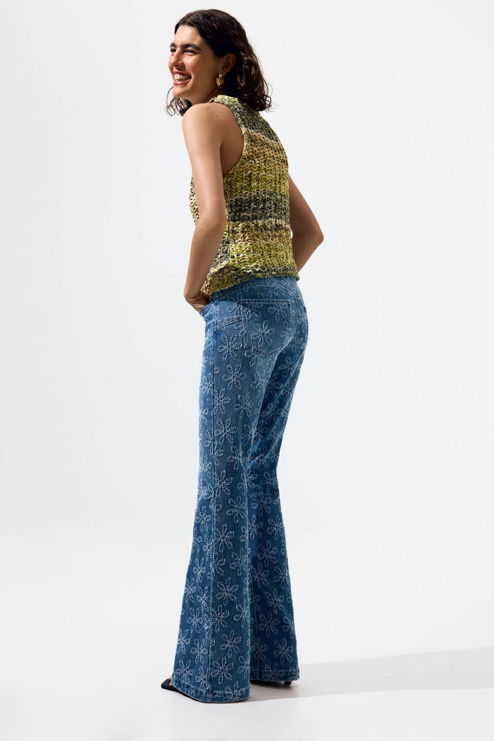 Femme portant une camisole en tricot texturé sans manches avec un pantalon en denim à motif fleuri.