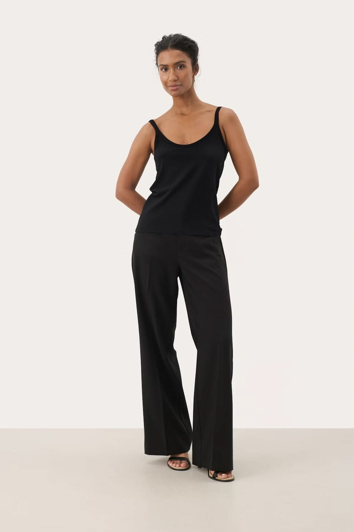 Femme portant une camisole à encolure arrondie noire avec bretelles fines et pantalon large, élégance et confort pour diverses occasions.