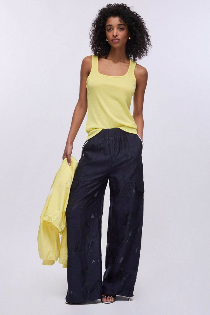 Femme portant une camisole à encolure carrée jaune, pantalon ample et veste assortie, montrant un look estival décontracté.
