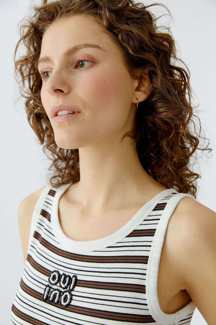 Femme portant une camisole à rayures avec maille côtelée et détail brodé subtile, silhouette moderne et bretelles larges.