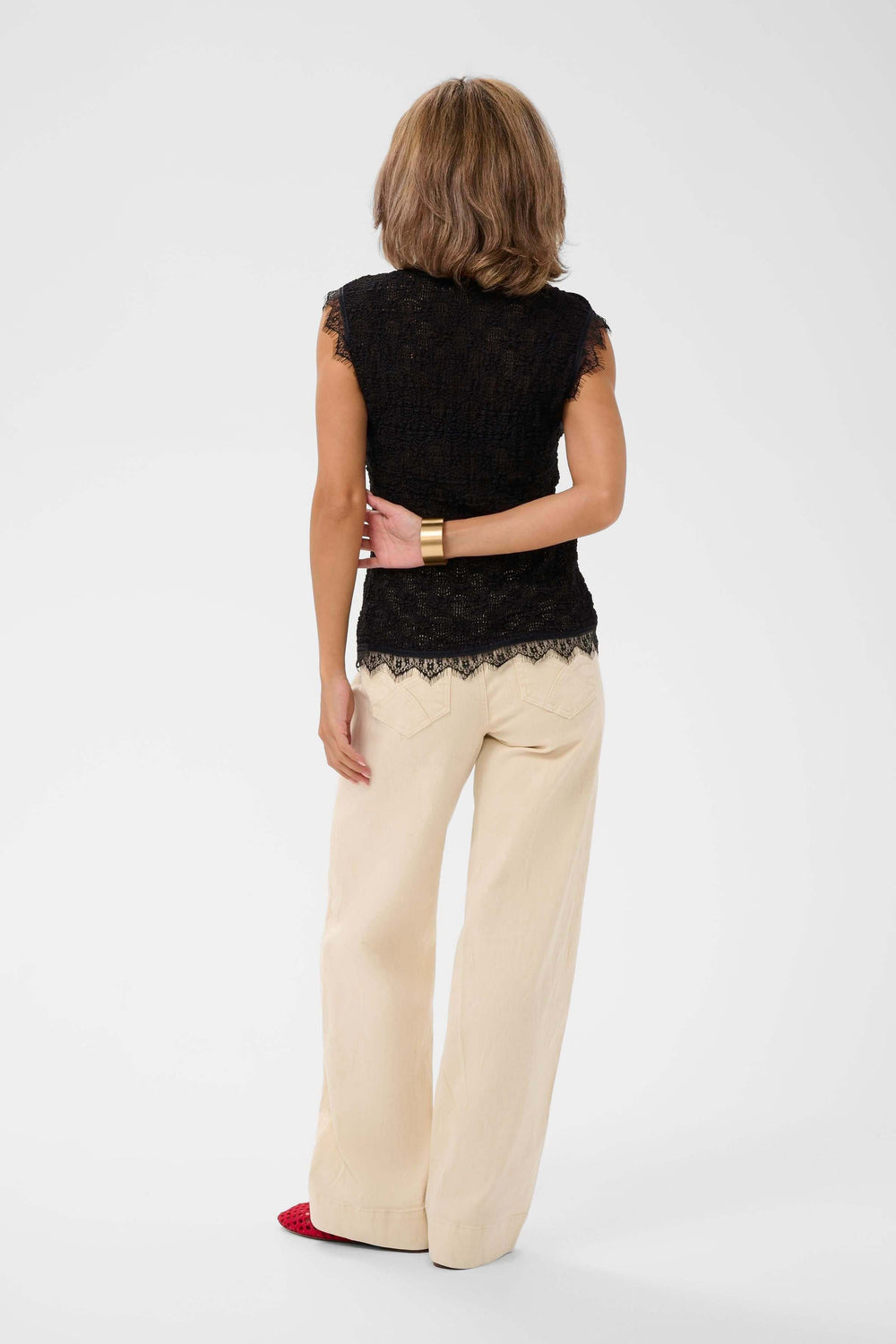 Femme portant une camisole sans manches en dentelle noire avec pantalon beige, vue de dos.