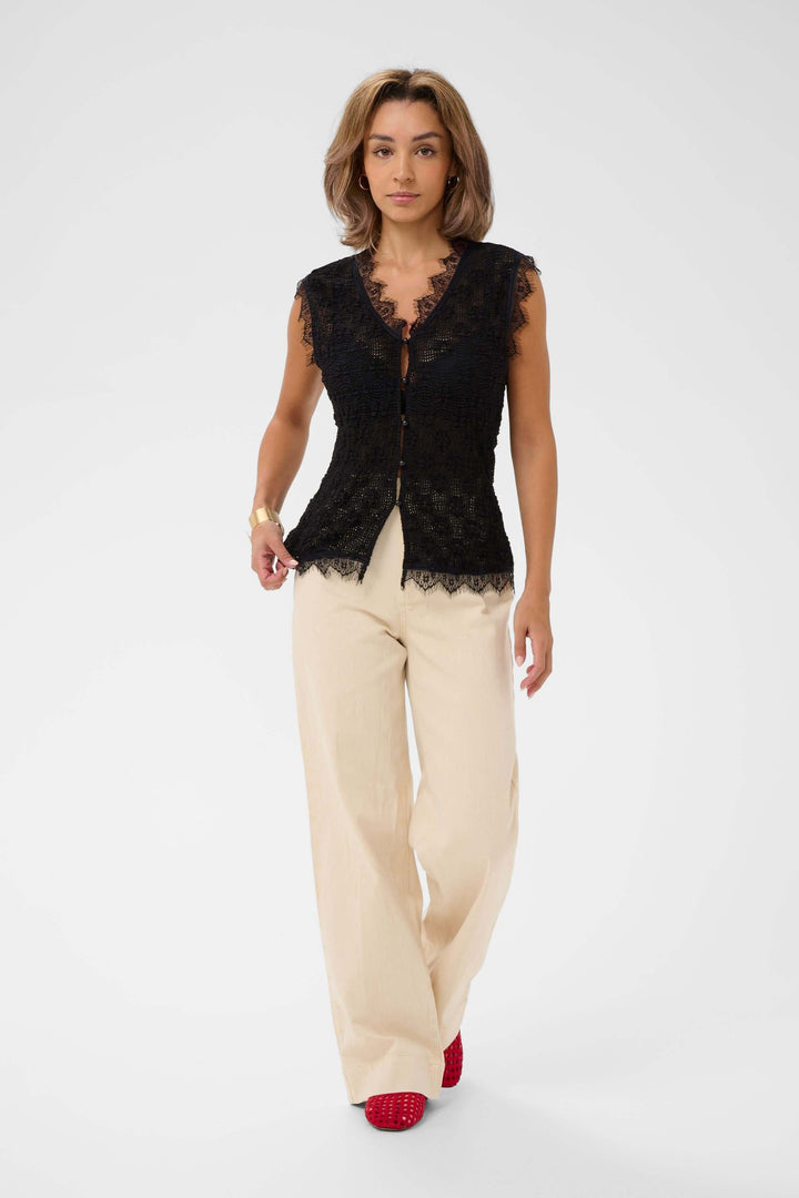 Femme portant une camisole sans manches en dentelle, élégante et féminine, avec des bordures festonnées et fermeture boutonnée.