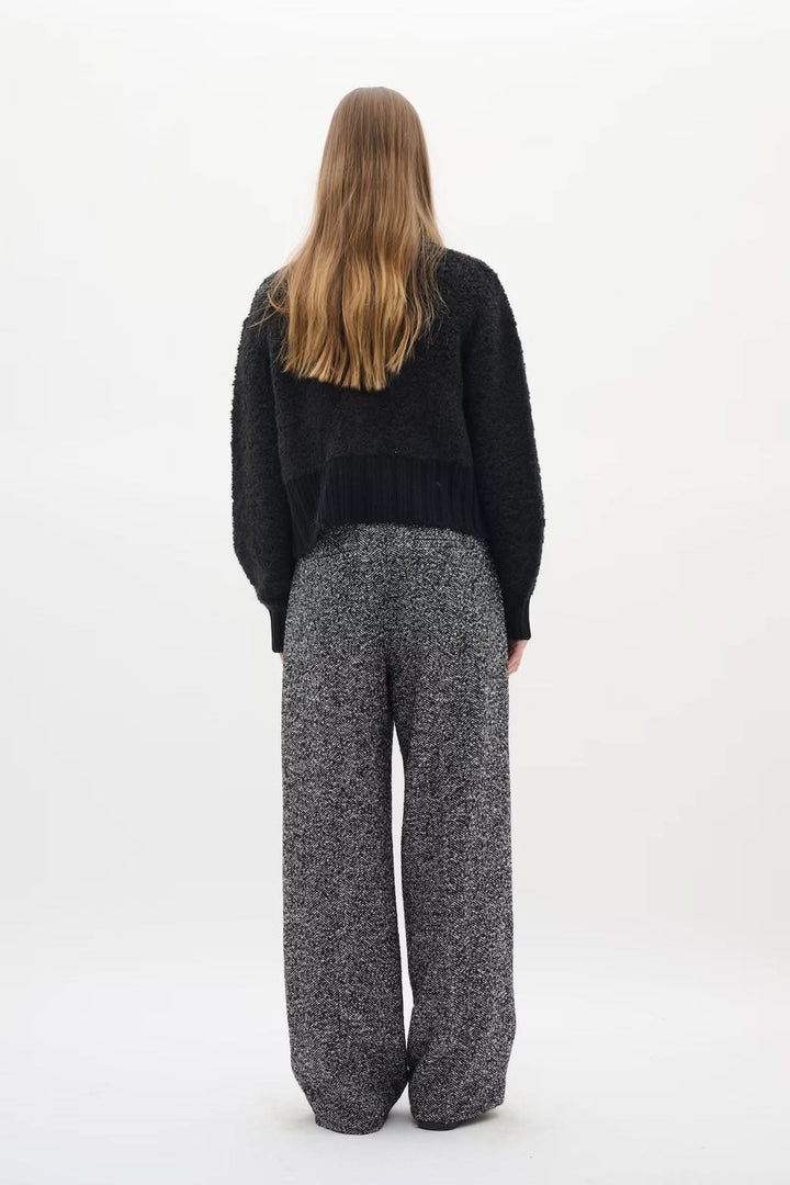 Dos d'une femme portant le Cardigan Guo noir, coupe courte structurée, avec pantalon large gris. Élégance moderne et sophistiquée.