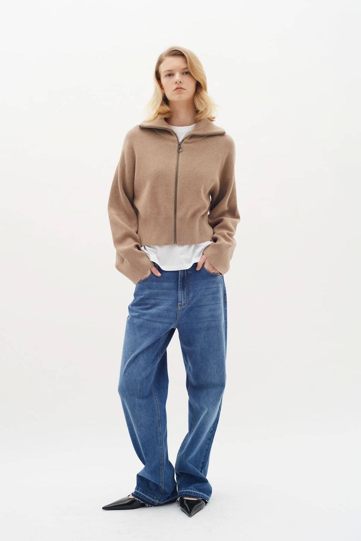 Modèle portant un cardigan beige à fermeture zippée, avec t-shirt blanc et jean, style décontracté et élégant.