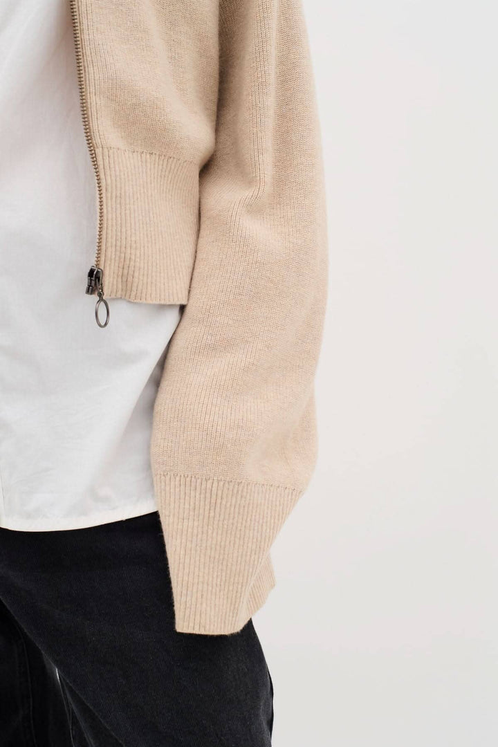 Détail d'un cardigan Jogan beige avec fermeture zippée, porté sur un t-shirt blanc et jean noir, style décontracté.