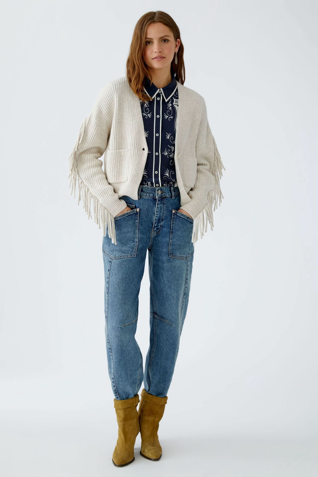 Cardigan avec franges in beige, porté avec une chemise imprimée et un jean, parfait pour un look décontracté.
