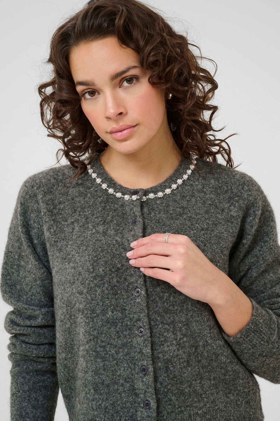 Femme portant un cardigan en laine bouclée à col orné de perles et strass, avec coupe droite et texture douce, style élégant classique.