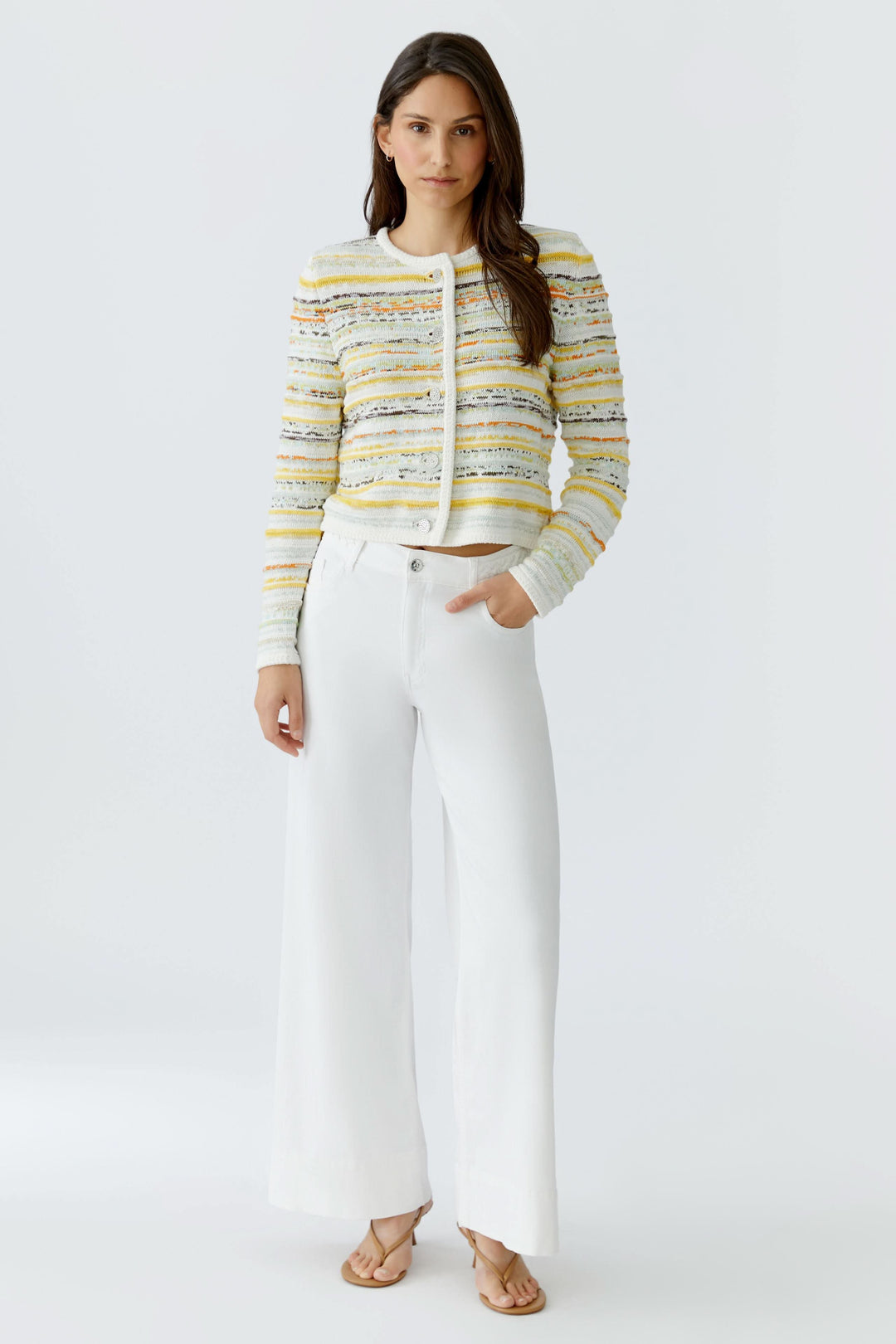 Cardigan en maille à rayures boutonné porté avec un pantalon blanc, offrant une allure élégante et structurée.