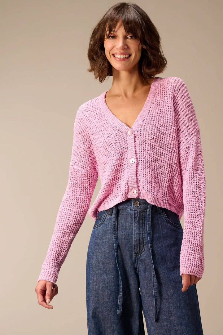 Femme portant un cardigan en maille texturée à col en V rose avec des finitions côtelées et fermeture boutonnée, look décontracté.
