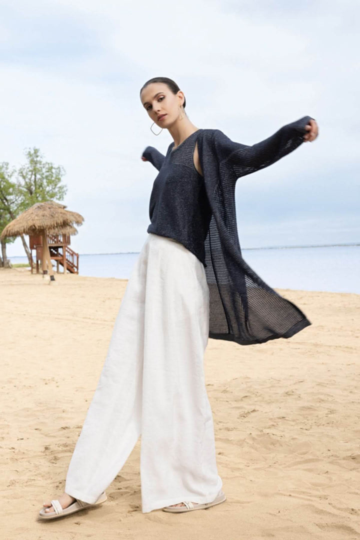 Femme portant un cardigan fluide ajouré et une camisole minimaliste sur la plage.