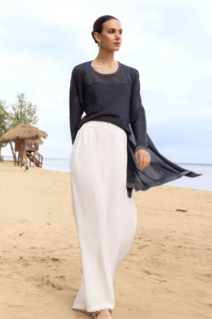 Femme portant un cardigan fluide ajouré et un pantalon blanc sur la plage, idéale pour les journées ensoleillées et soirées douces.
