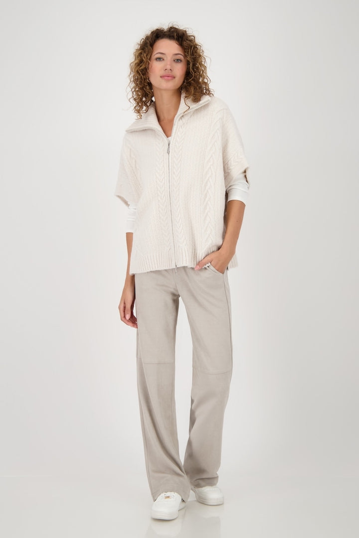 Cardigan en maille torsadée oversize avec col roulé et fermeture éclair, porté avec un pantalon clair.