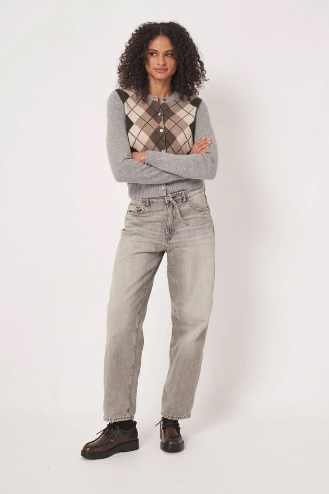 Cardigan à motif losanges sur un fond gris, porté avec un jean et des bottines, style moderne et rétro.