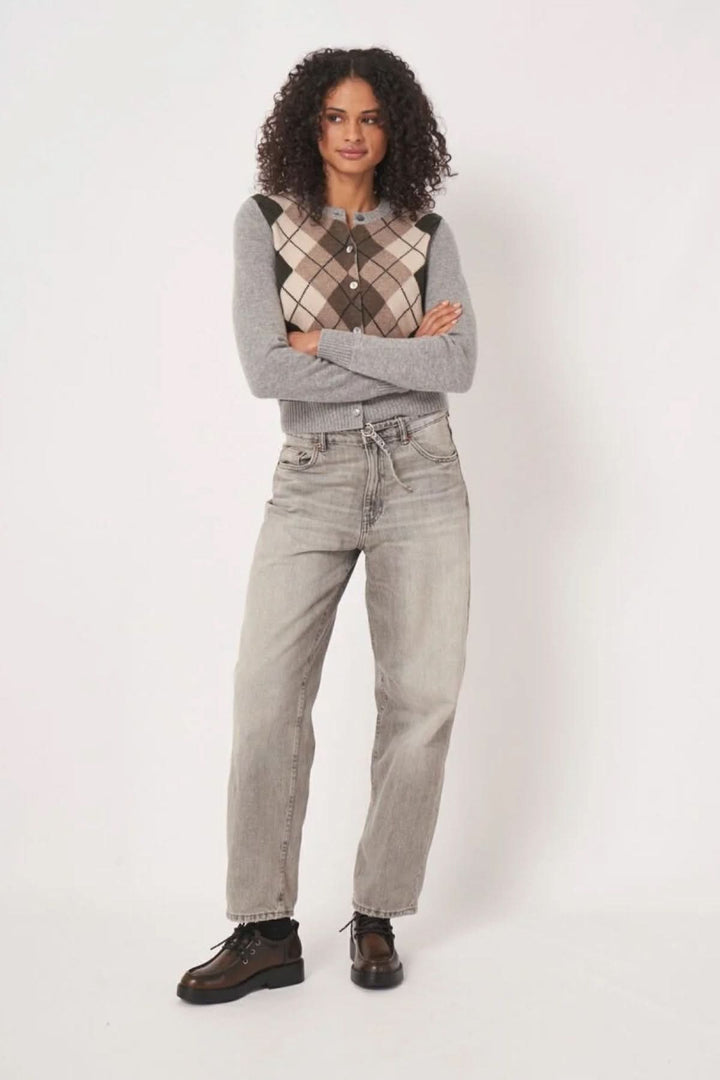 Cardigan à motif losanges sur un fond gris, porté avec un jean et des bottines, style moderne et rétro.