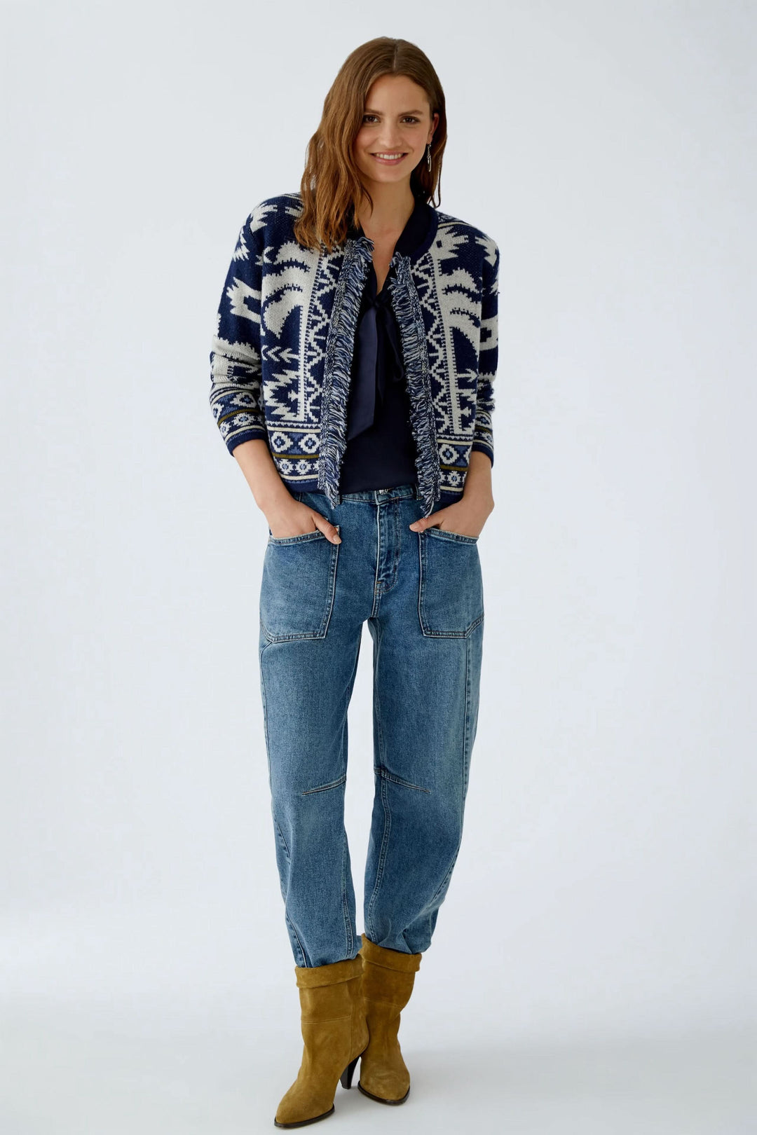 Femme portant un cardigan motif western en jacquard avec franges, jeans décontractés et bottes en cuir.
