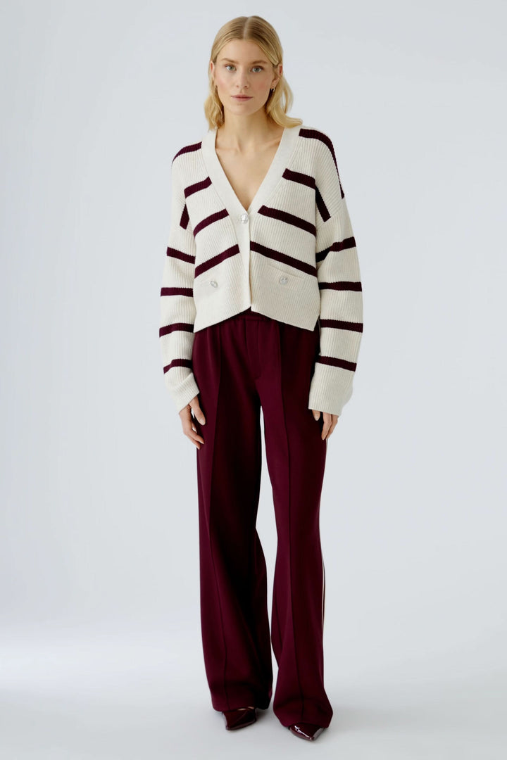 Femme portant un cardigan à rayures modernes avec une encolure en V et un pantalon fluide bordeaux.