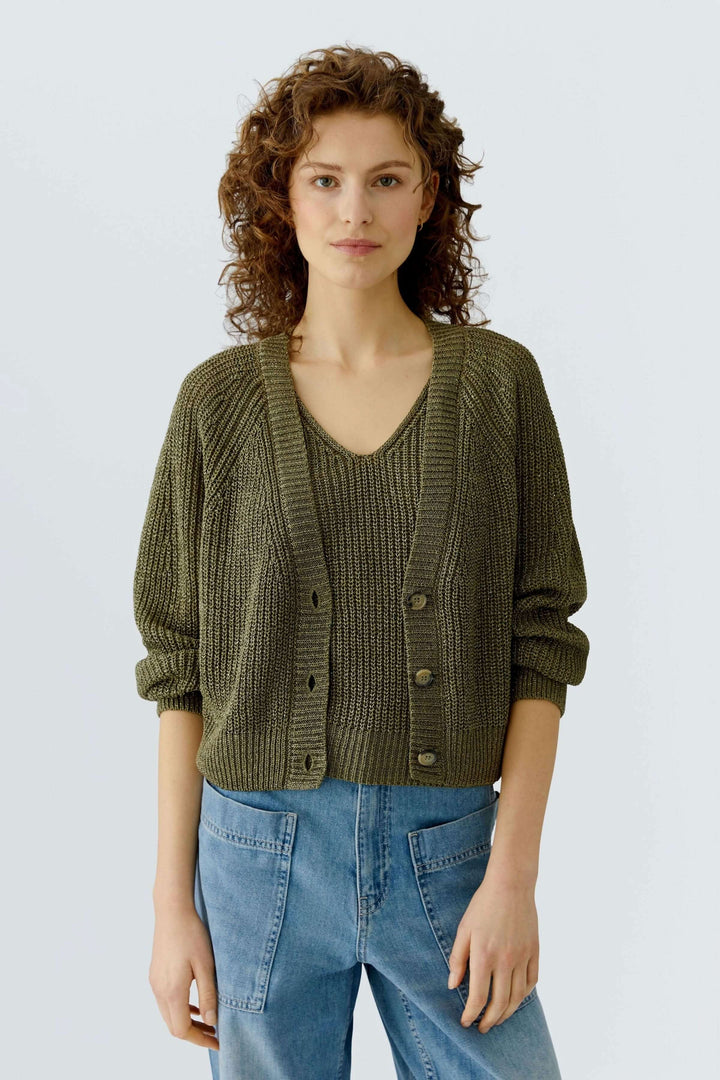 Femme portant un cardigan tricoté en maille de couleur kaki avec une encolure en V et fermeture boutonnée, coupe courte et droite.