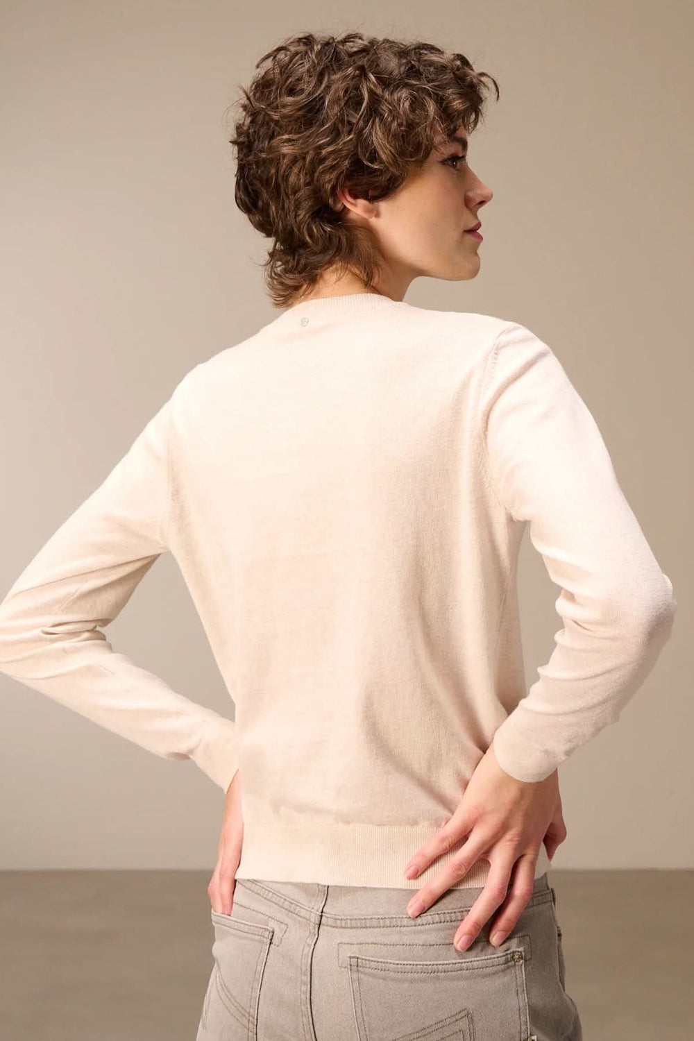 Vue arrière d'un cardigan tricot fin boutonné col rond avec manches longues, porté par une personne, coupe ajustée en couleur claire.