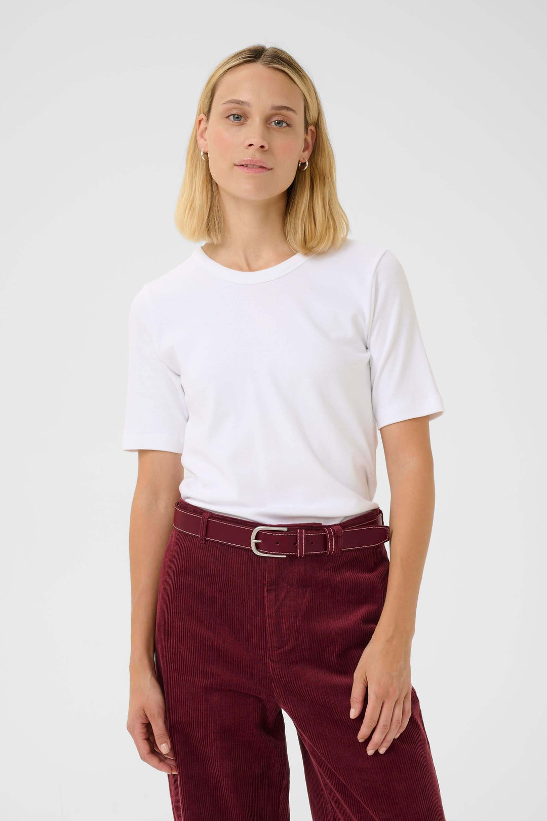 Femme portant une ceinture en cuir seyra, tee-shirt blanc et pantalon bordeaux, style chic et intemporel.