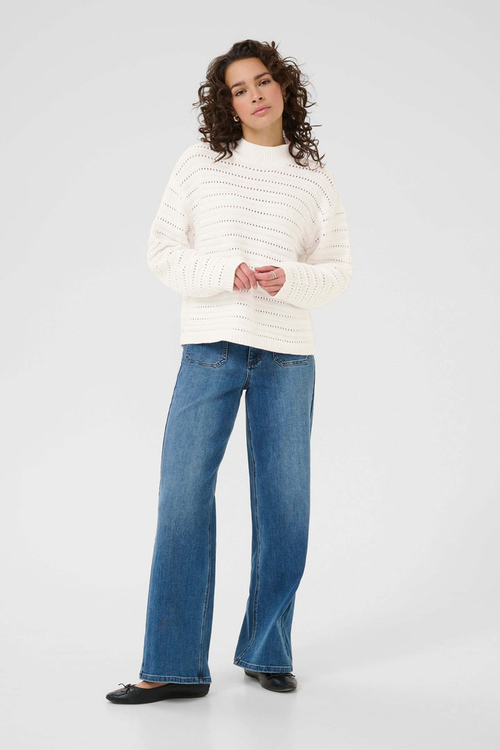 Chandail Dolly en tricot ajouré élégant avec col montant, porté avec un jean pour un style moderne et chic.