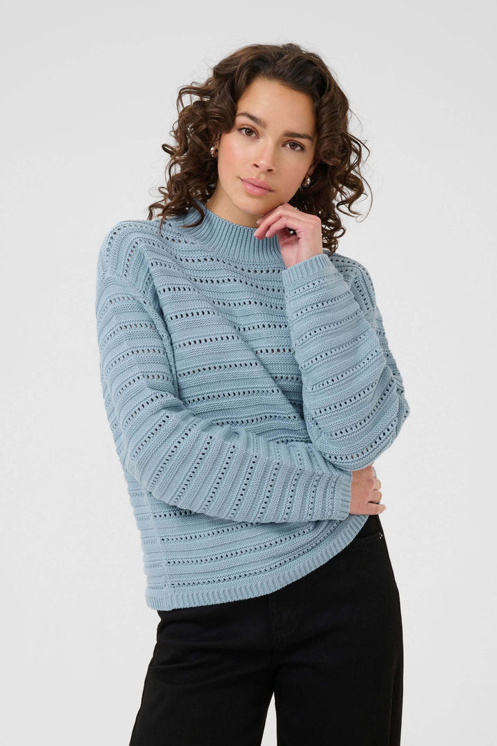 Femme portant le Chandail Dolly en tricot ajouré bleu avec col montant, style chic et polyvalent.