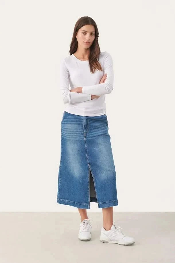Femme portant un chandail blanc ajusté et une jupe en denim.