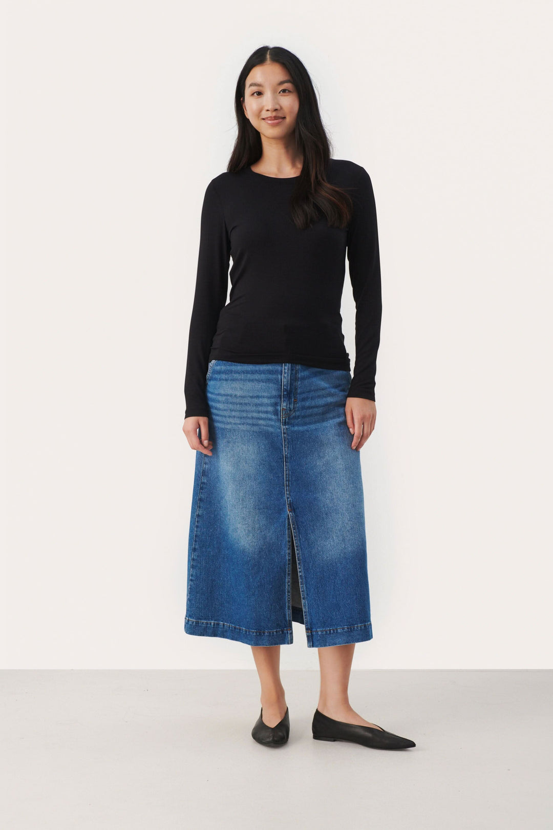 Femme portant un chandail noir ajusté et une jupe en jean bleue, look élégant et décontracté.