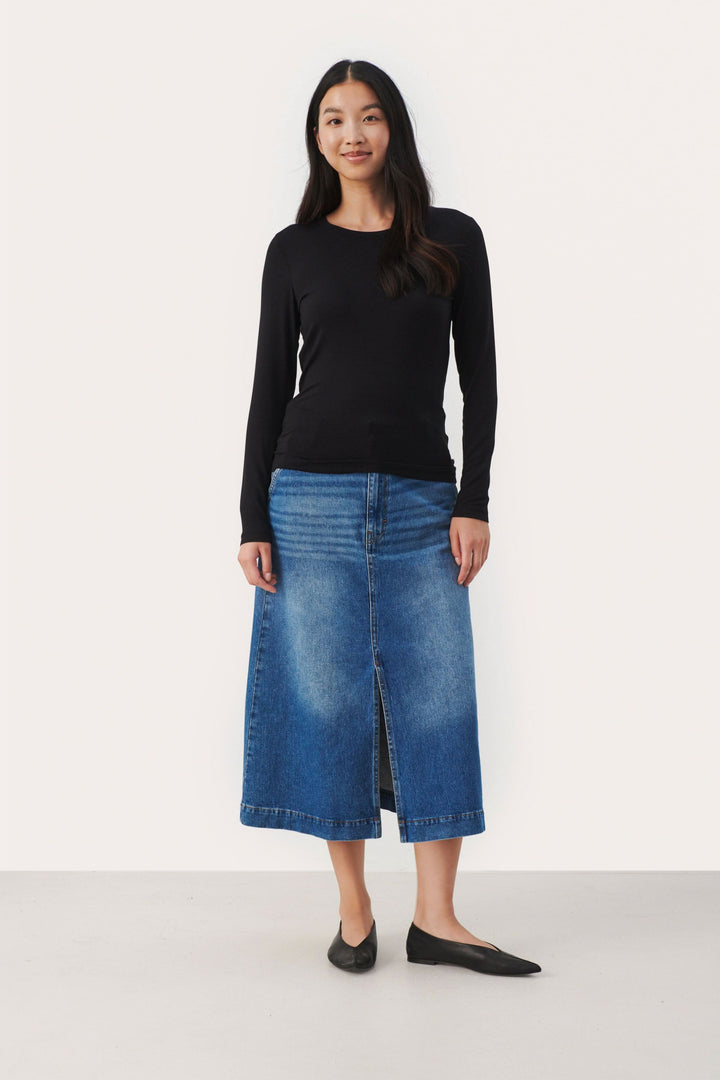 Femme portant un chandail noir ajusté et une jupe en jean bleue, look élégant et décontracté.