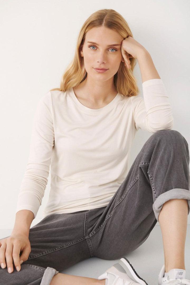 Chandail Emaja beige à manches longues, encolure ronde, porté avec un pantalon gris, style décontracté.