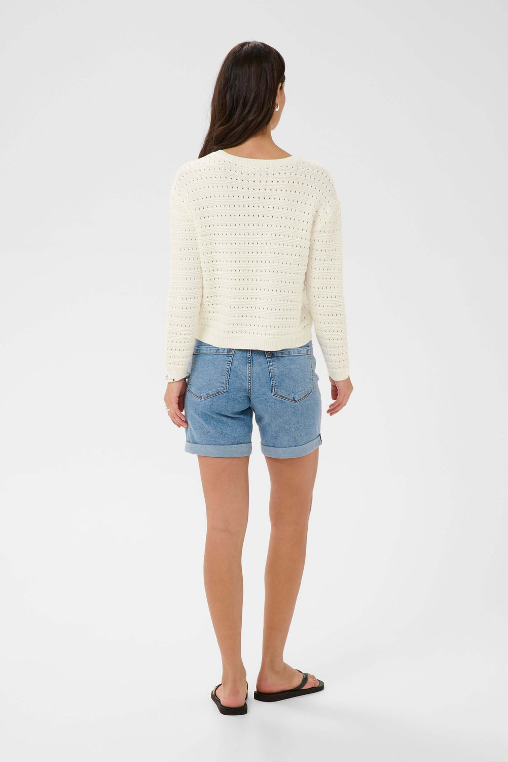 Femme portant le Chandail Metta en maille ajourée blanche, vue de dos, avec short en jean.