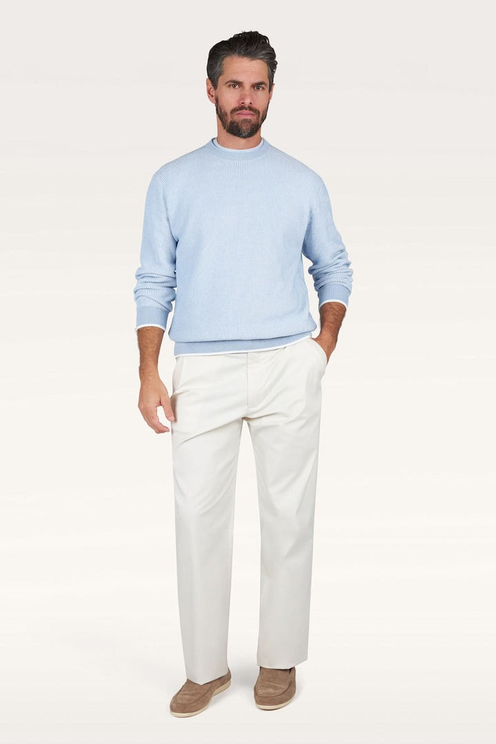 Homme portant un Chandail Piuma en coton ultraléger bleu avec pantalon blanc, représentant une mode élégante et contemporaine.