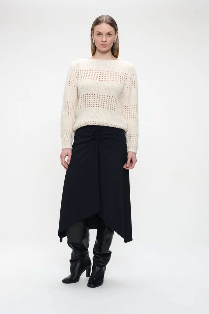 Femme portant un "Chandail ajouré à encolure ronde" crème avec une jupe noire et des bottes noires, style moderne et chic.