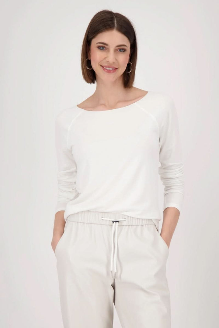 Femme portant un chandail basique blanc à manches longues, coupe cintrée, col rond, et pantalon assorti.