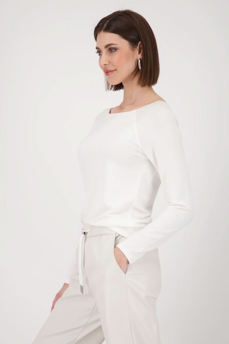 Femme portant un chandail basique blanc à manches longues, coupe légèrement cintrée, col rond classique, idéal pour diverses occasions.