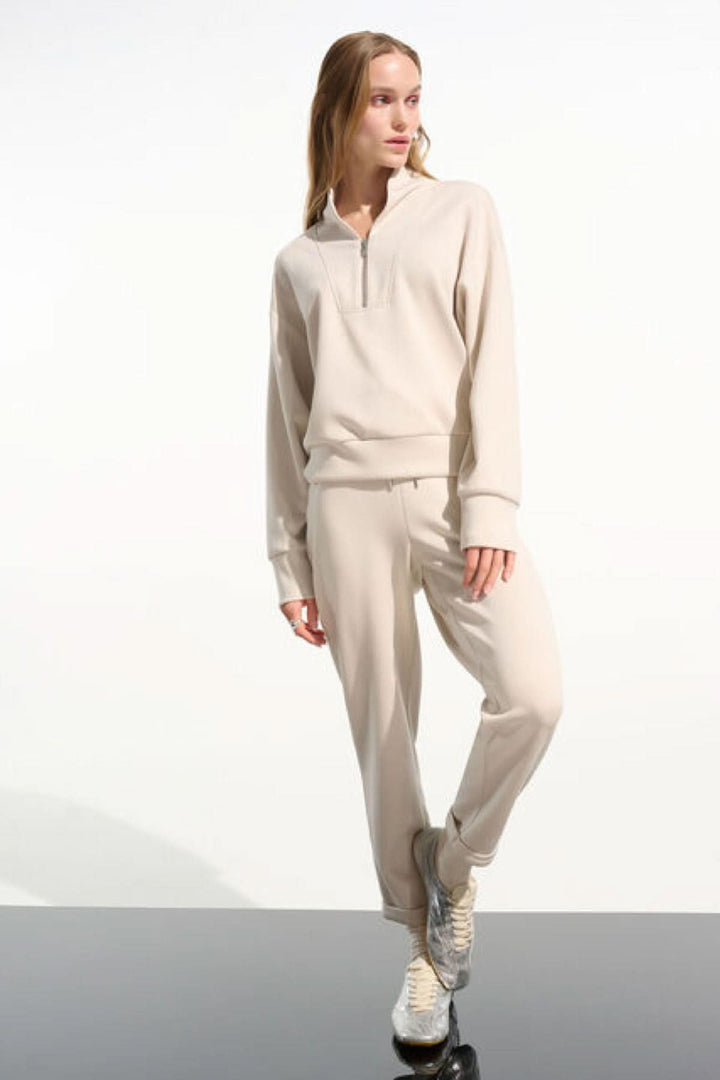 Chandail à col montant beige avec fermeture demi-zip, coupe fluide et manches longues, porté par un mannequin pour un style moderne.