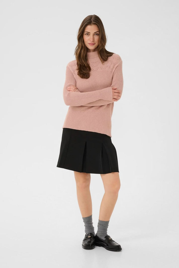 Chandail à col montant rose avec jupe noire pour un look moderne et raffiné.