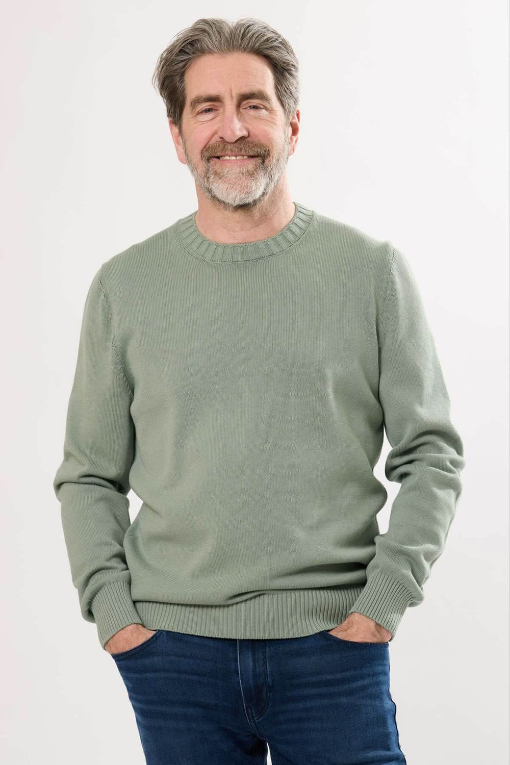Homme souriant portant un chandail à col rond vert près du corps, parfait pour un look décontracté et élégant.