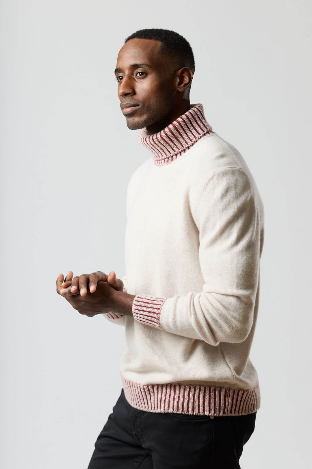Homme portant un chandail col roulé à côtes contrastées, style moderne et élégant, fond blanc.