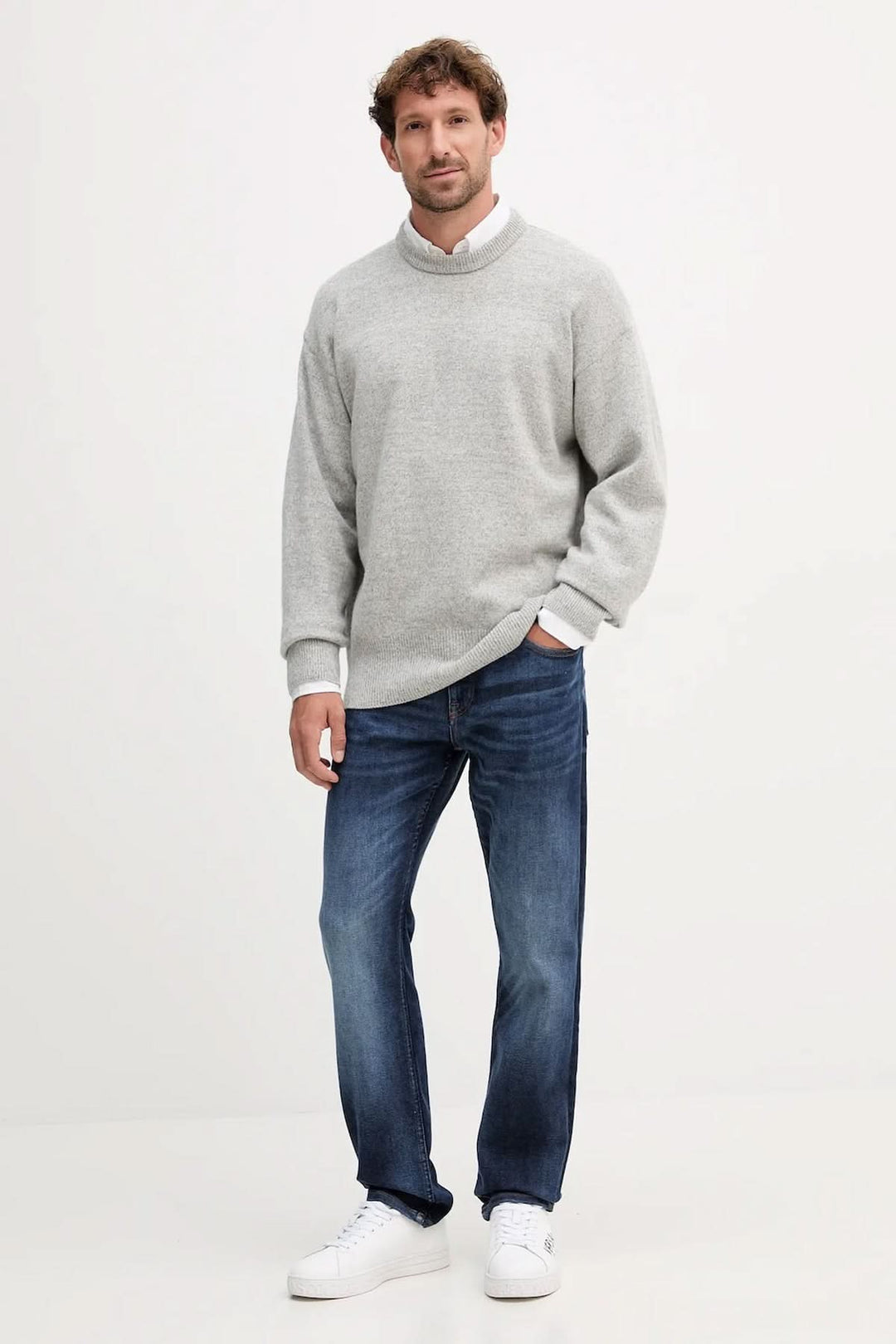 Homme portant un chandail en laine vierge coupe "oversize" BOSS de couleur grise, avec jean et baskets blanches.